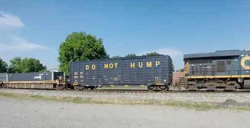 an american freight train with a black boxcar with yellow all caps lettering that says "DO NOT HUMP"