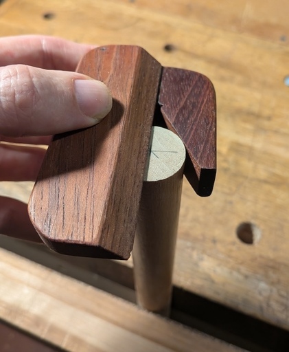 A shop-made wooden center finder being used on the end of a dowel