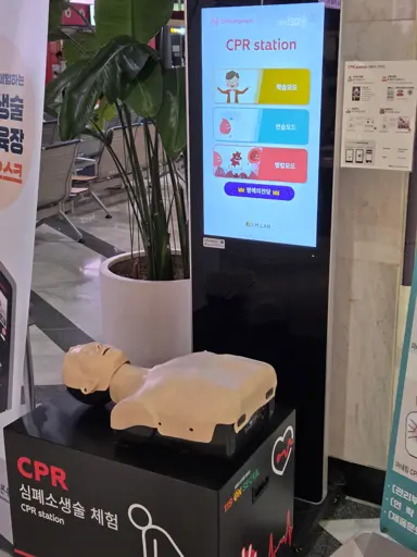 A kiosk-like machine with a CPR practice doll in front of it.